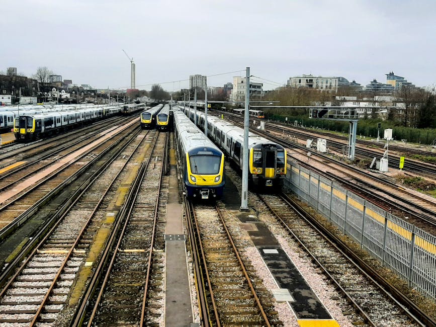 A modern commuter train is stationary at West Ham station platform, with its sleek, silver exterior featuring red accents along the carriages. The platform is partially covered by a roof with a metal 